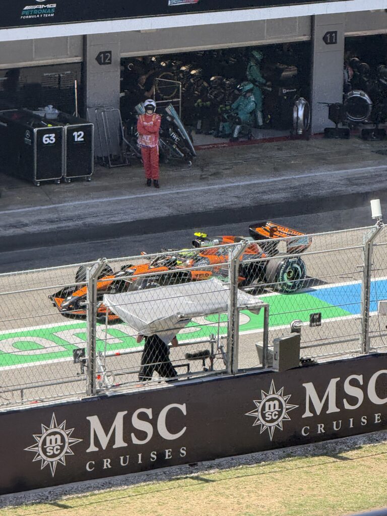 Lando Norris driving his orange McLaren Formula 1 car through the pit lane at the 2025 Barcelona Grand Prix