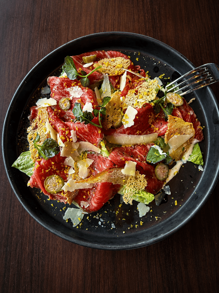 Imperial Farms Wagyu carpaccio with baby gem lettuce, caperberries, croutons, Parmesan, and Caesar dressing at Peak NYC