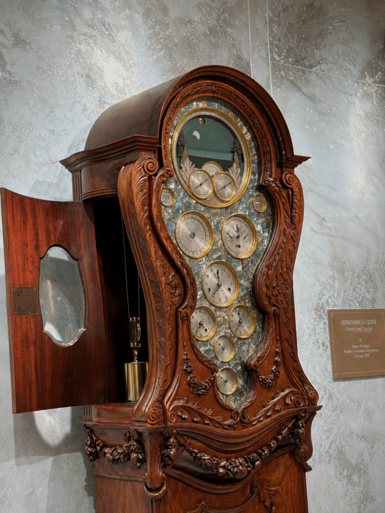 Ornately carved Tiffany astronomical grandfather clock with multiple dials, a moon display and exposed pendulum mechanism