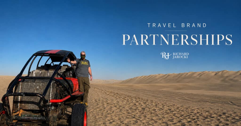 Richard Jarocki standing beside a desert buggy in the sand dunes beneath a clear blue sky for his travel brand partnerships page.