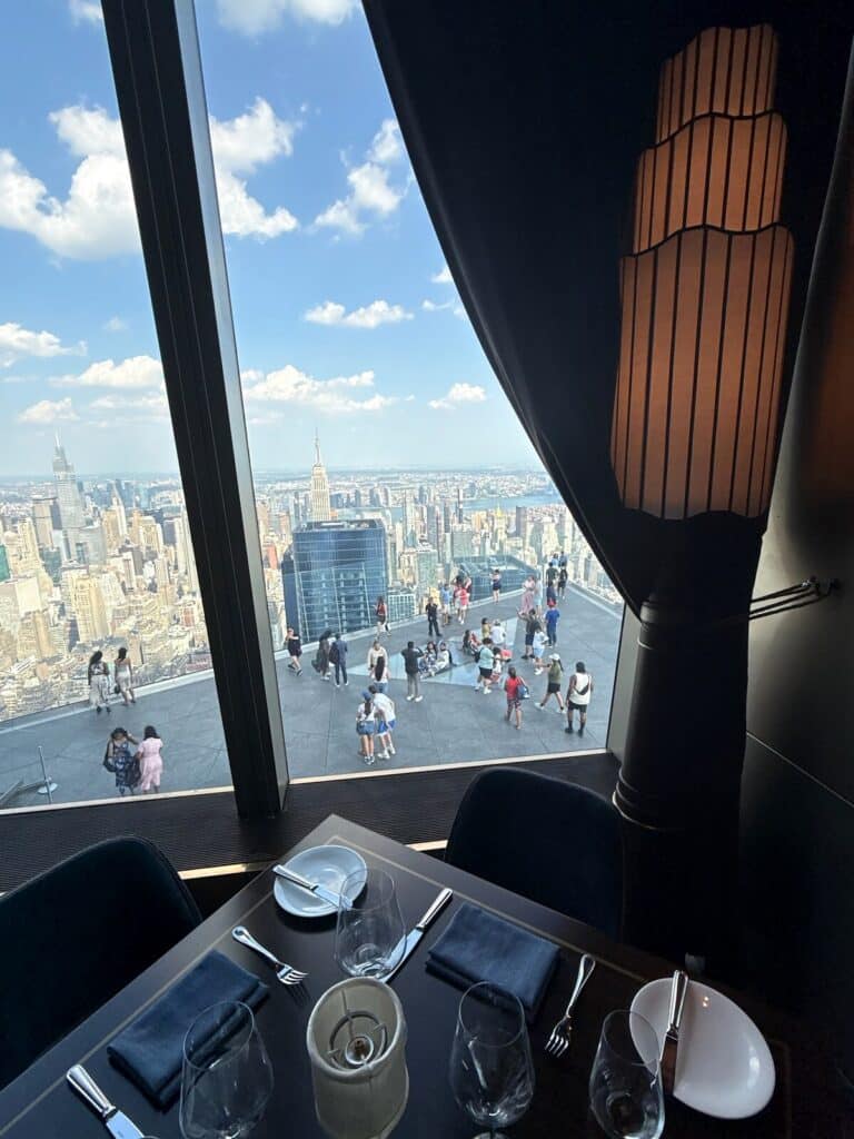 View of The Edge NYC observation deck and Manhattan skyline from a table inside Peak Restaurant
