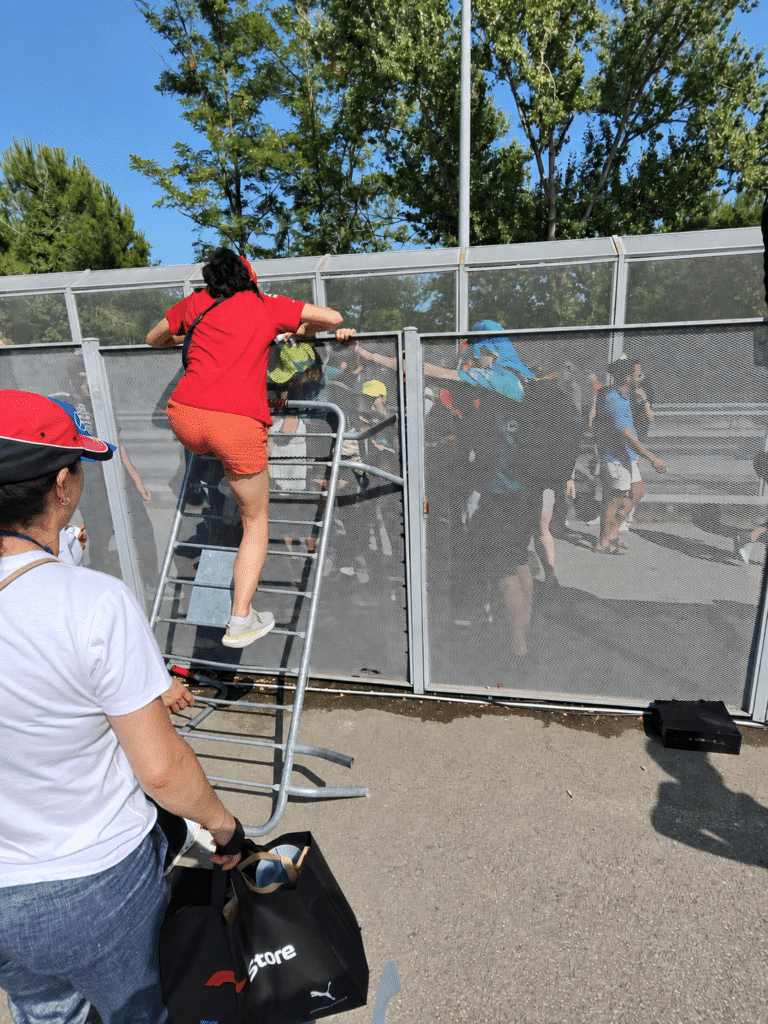 Why I Love Formula 1 Spectators helping one another cross a circuit fence using a metal divider in Barcelona.