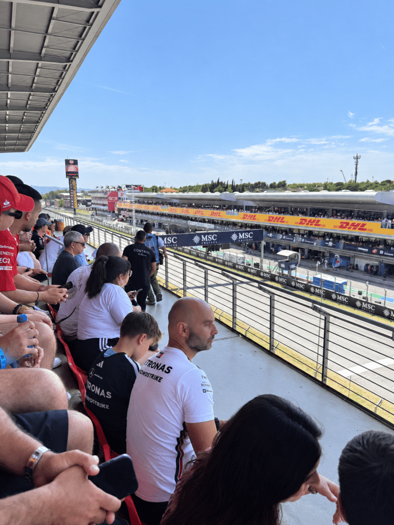 Fans seated in a Barcelona grandstand overlooking the main straight and pit building.