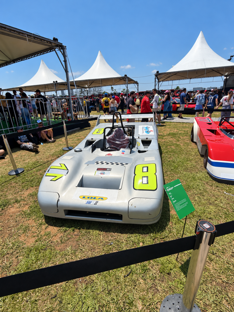 A silver Lola racing car with a bright number 8 displayed beside another racing car and white tents.