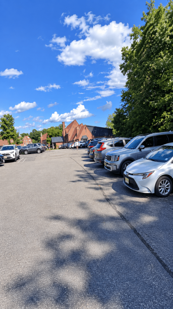 Parking area leading toward Drowned Lands Brewery in Warwick, with trees and a blue sky.
