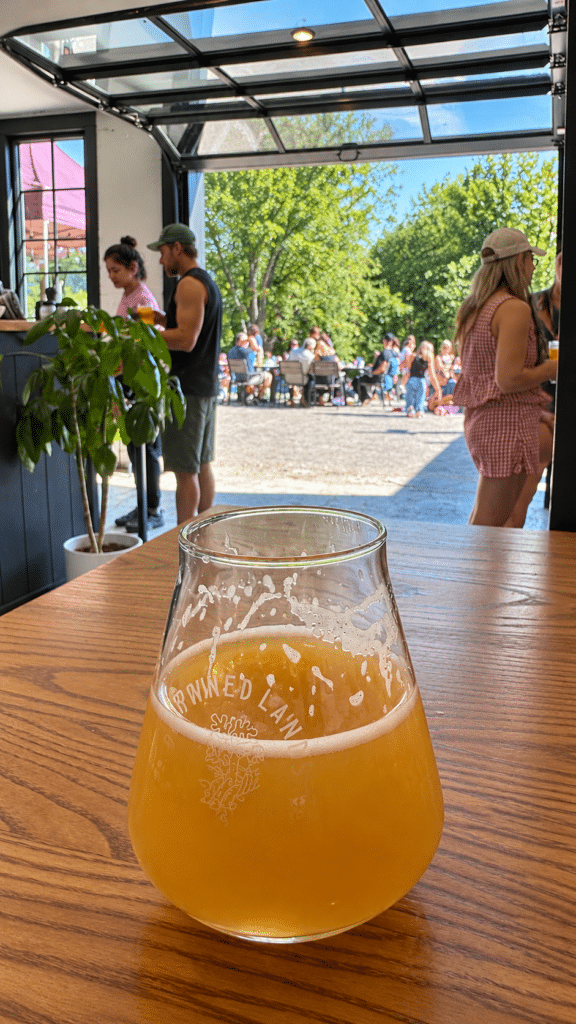 Glass of Deep Terra beer on a wooden table at Drowned Lands Brewery, with open doors overlooking outdoor seating.