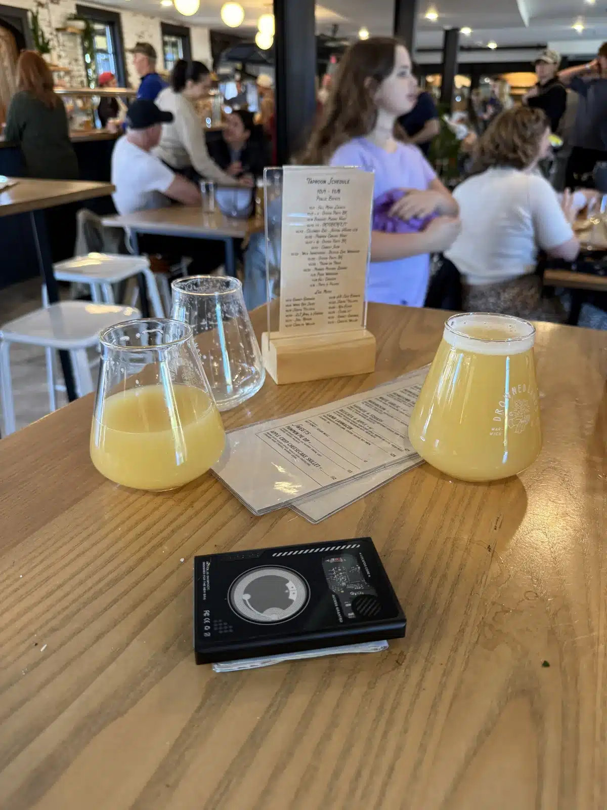 Beer glasses and a LORZOR wallet on a wooden table inside the Drowned Lands taproom
