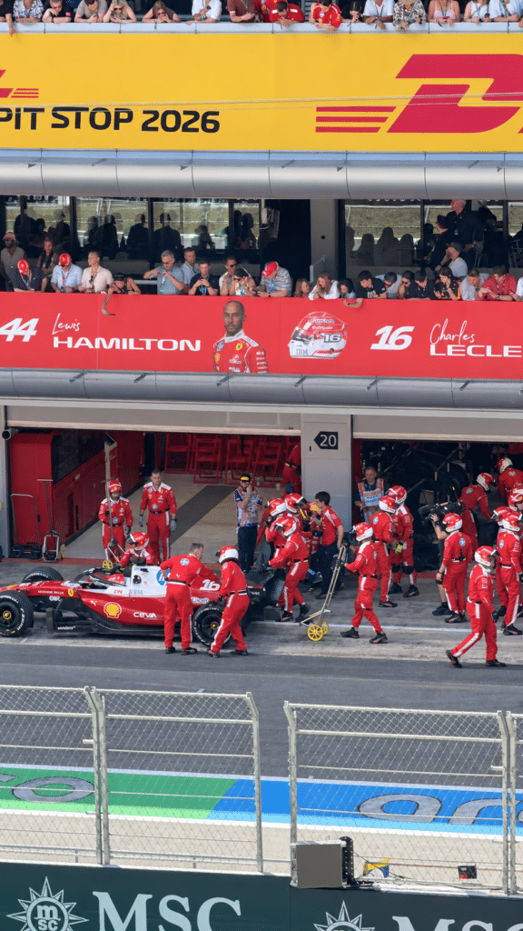 Why I Love Formula 1 Ferrari mechanics working around a car outside garages marked for Lewis Hamilton and Charles Leclerc.