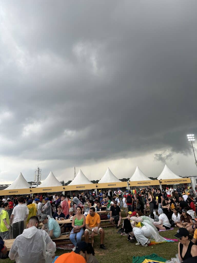 Why I Love Formula 1 Dark storm clouds above fans in rain ponchos gathered at picnic tables and food stalls at Interlagos.