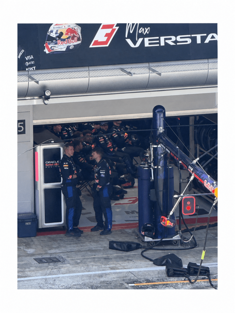 Red Bull team members and pit equipment beneath Max Verstappen’s garage signage in Barcelona.
