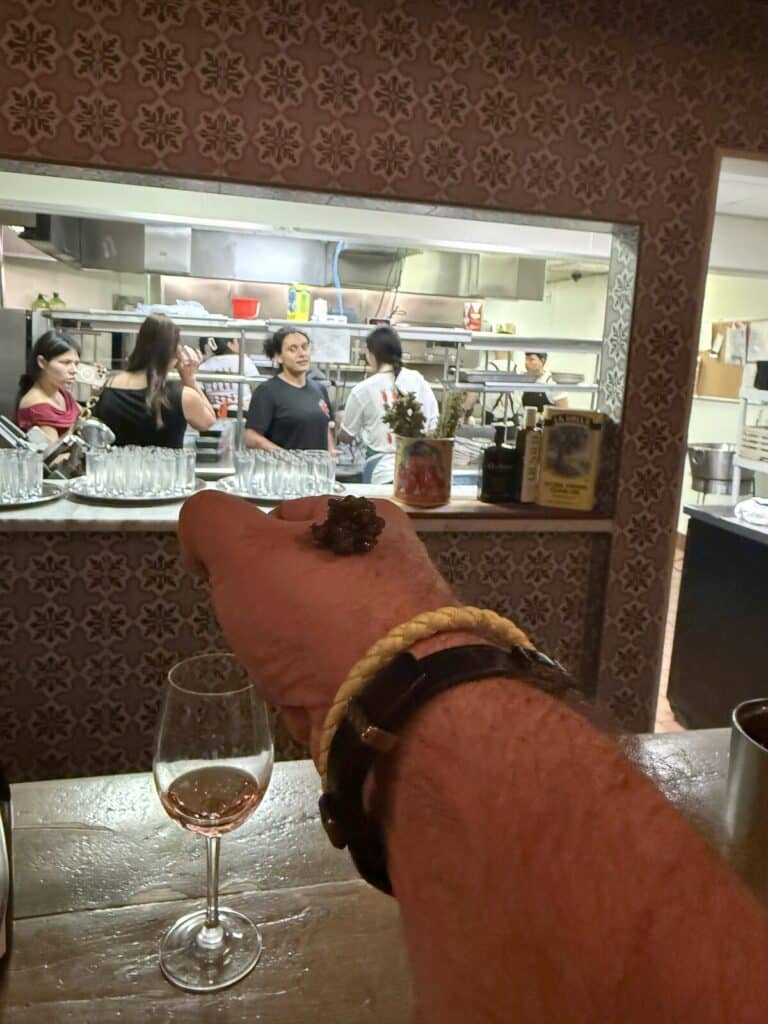 A serving of caviar on the back of a hand, with a wine glass and Viaggio's open kitchen behind.