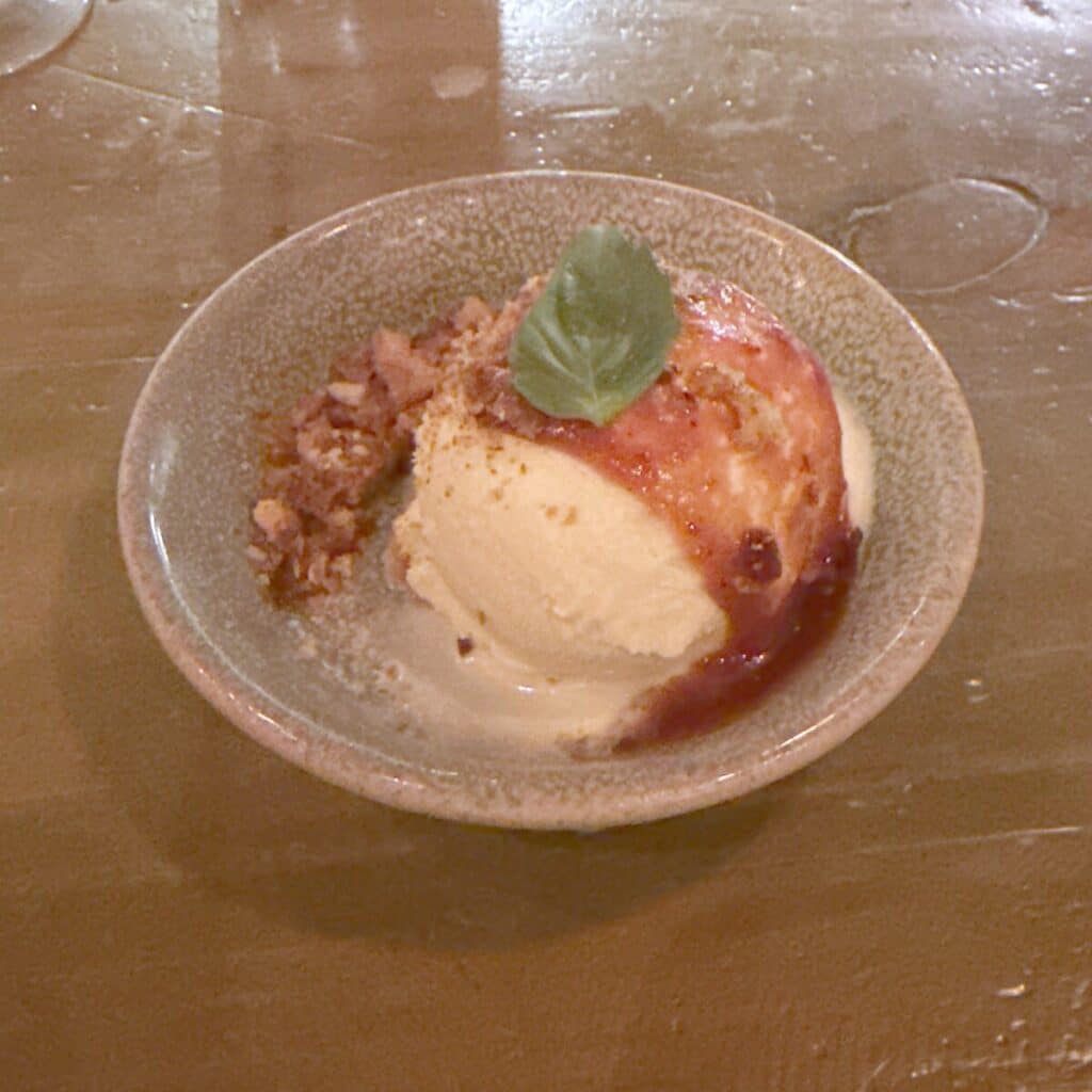 Fior di latte gelato topped with tomato jam and basil, with focaccia crumble in a ceramic bowl.
