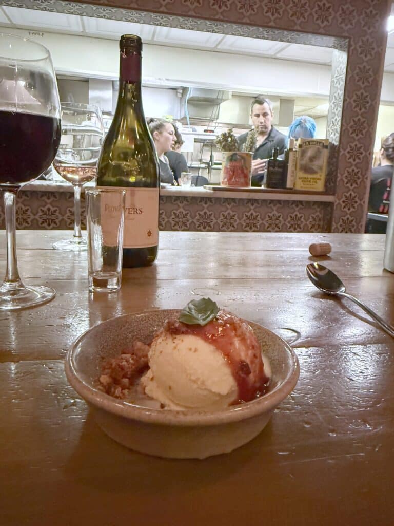 Italian Sundae on Viaggio's wooden counter, with wine glasses, a Flowers bottle and the open kitchen behind it.