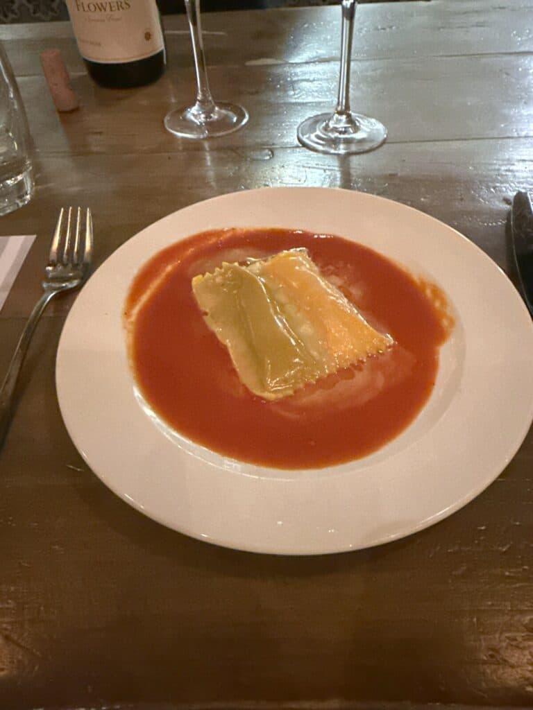 Overhead view of Raviolo Doppio alla Norma in tomato sauce on a white plate at Viaggio.