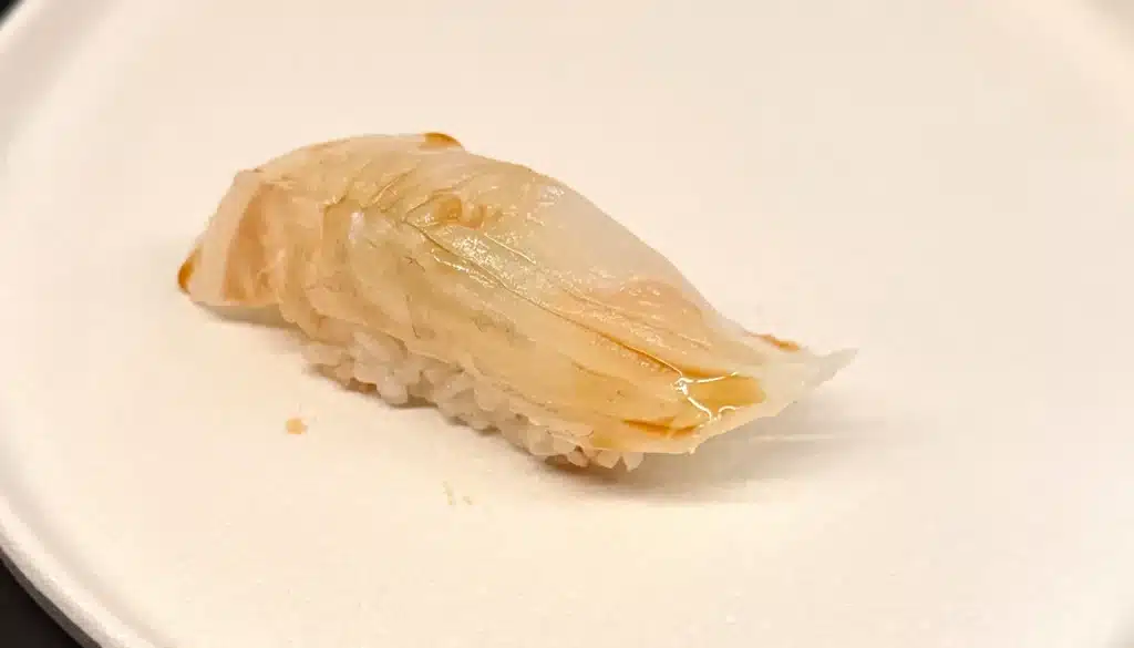 Sushi by Sea Review Pale fluke nigiri with a glossy, scored surface over rice.