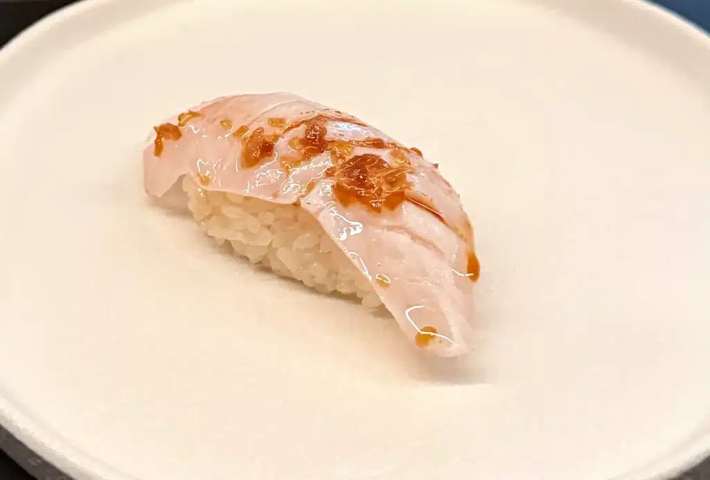 Sushi by Sea Review Pale madai nigiri with browned patches on top and rice visible beneath.
