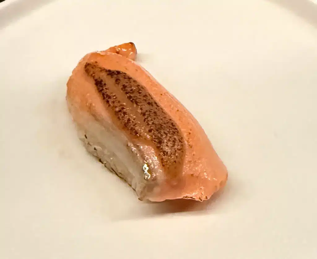 Sushi by Sea Review Orange salmon nigiri with a dark seared stripe across the top.