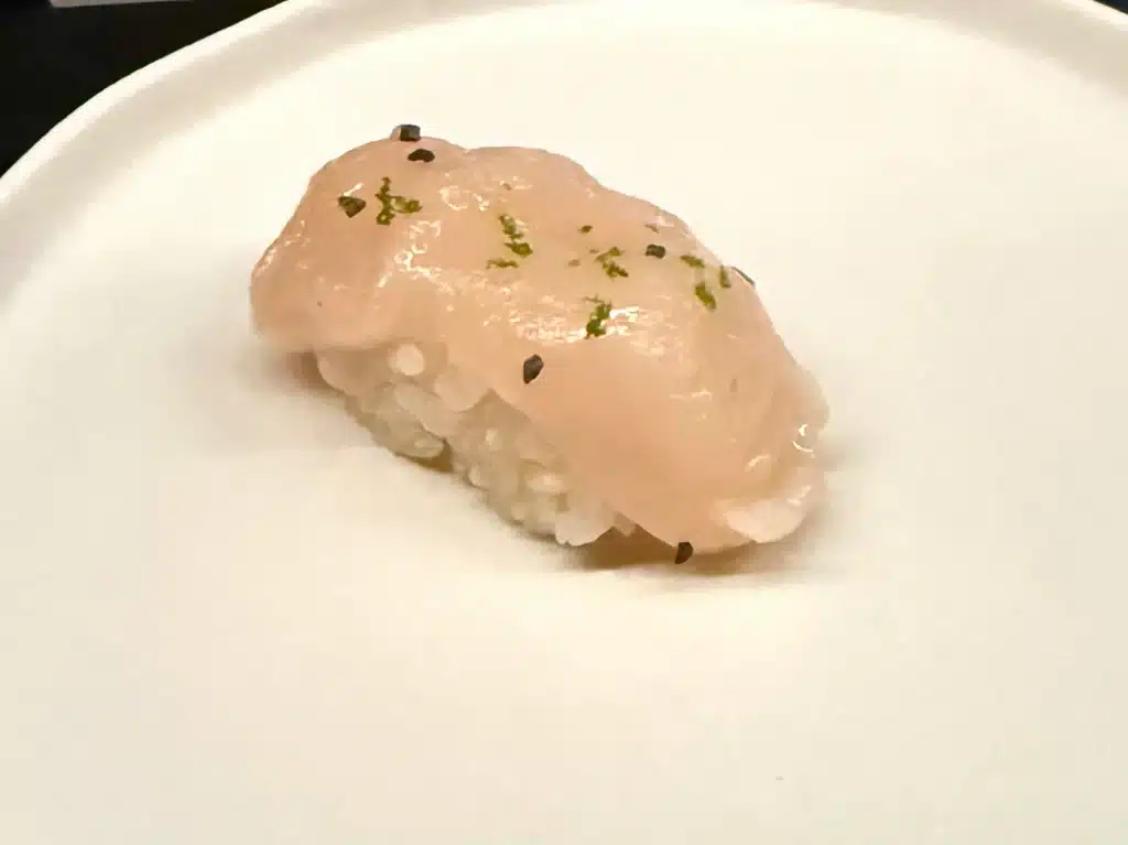 Sushi by Sea Review Pale Hokkaido scallop nigiri with green and dark flecks over rice.