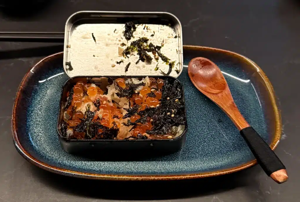 Sushi by Sea Review Open mini ikura bento box with orange roe and dark shredded garnish over rice.