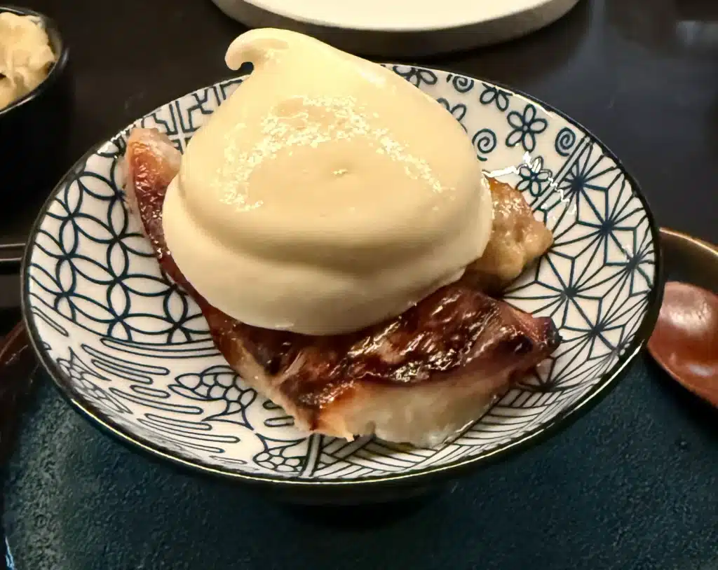 Sushi by Sea Review Browned cod beneath a large mound of pale foam in a blue-and-white patterned bowl.