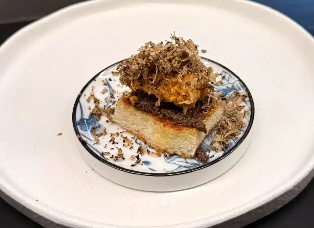 Sushi by Sea Review  A square of milk bread topped with orange uni and a mound of truffle shavings.
