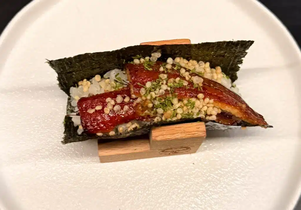Sushi by Sea Review Glazed eel over rice with green and pale garnishes, 