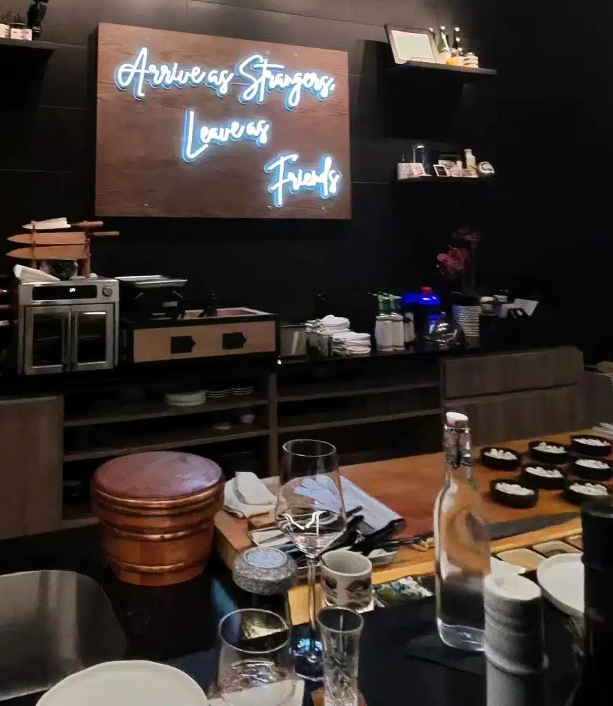 The neon “Arrive as Strangers, Leave as Friends” motto above the Sushi by Sea counter.