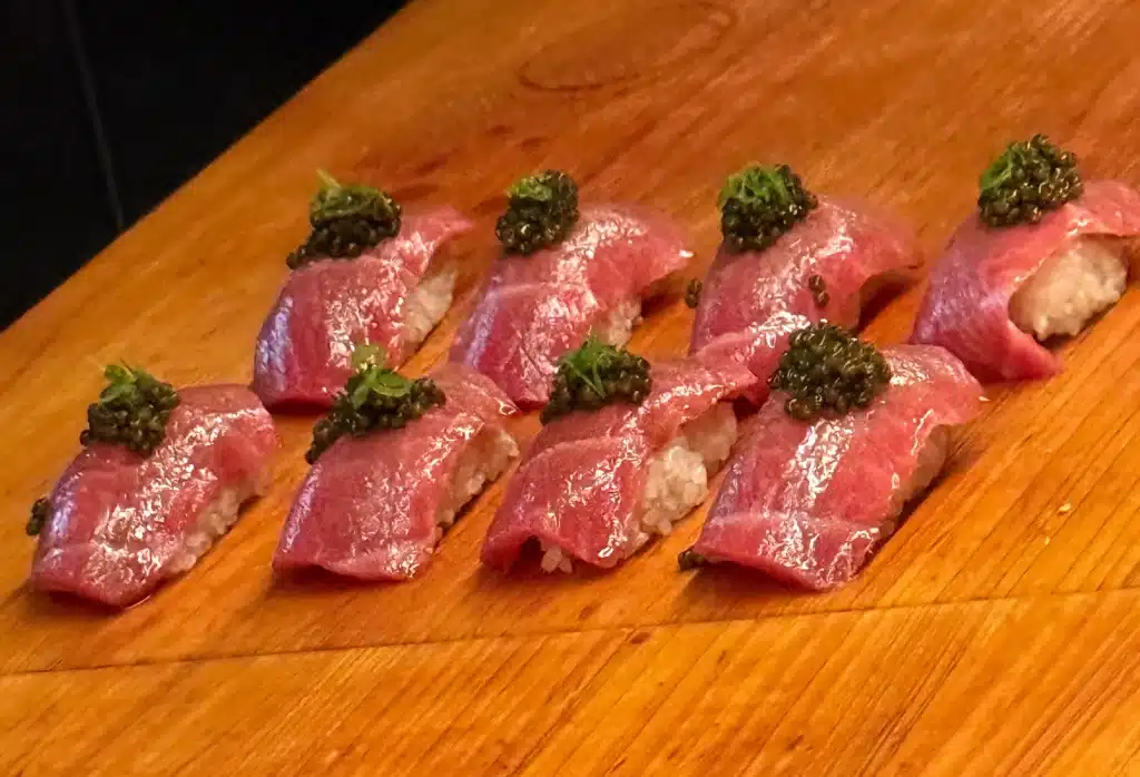 Rows of pink chutoro nigiri topped with caviar on the wooden counter.