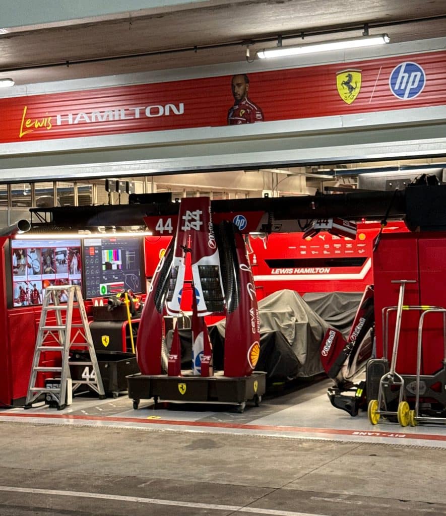 São Paulo Grand Prix Travel Guide Lewis Hamilton’s number 44 Ferrari garage at Interlagos, with spare front wings, a covered car and wet pavement outside.