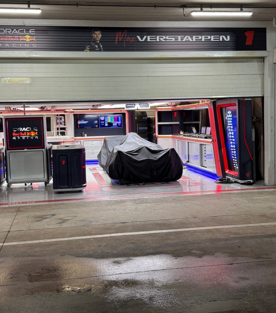 Max Verstappen’s number 1 Red Bull garage at Interlagos, with a covered car inside and reflections on the wet pit lane.