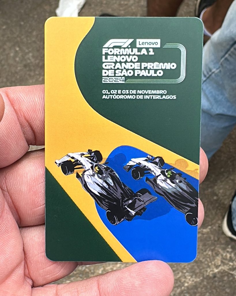 Richard Jarocki's hand holding a green, yellow and blue cashless payment card from the 2024 São Paulo Grand Prix, featuring two illustrated racing cars.